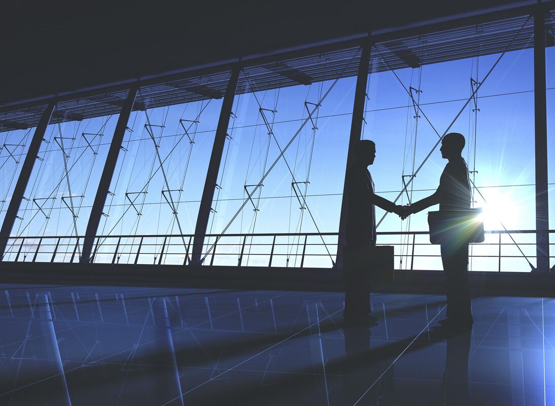 photo of two figures shaking hands, standing before a row of large windows with light that obscures their features in shadow